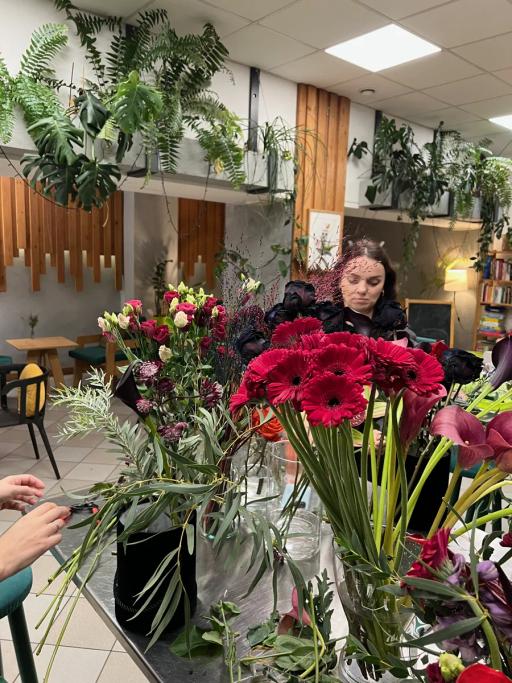 Kobieta uczestniczy w warsztacie florystycznym, tworząc bukiet z czerwonych gerber i innych kwiatów w nowoczesnej sali.