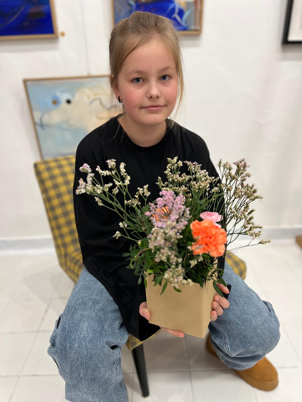 Dziewczyna w czarnej koszulce i dżinsach trzyma bukiet kwiatów w papierowym pojemniku.