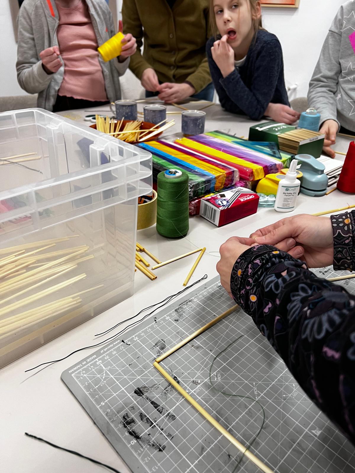 Dzieci uczestniczą w warsztacie rękodzielniczym, pracując z kolorowymi materiałami i narzędziami do tworzenia rękodzieła.