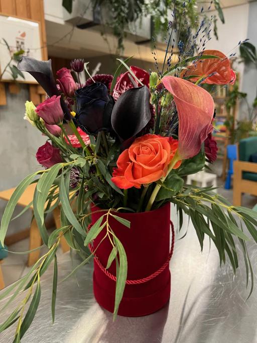 Elegancki bukiet kwiatów w bordowej tubie zawiera róże, kalie, goździki i dekoracyjne trawy.