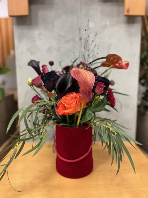 Elegancki bukiet kwiatów w bordowym wazonie na drewnianym stole zawiera róże, kalie i liście paproci.