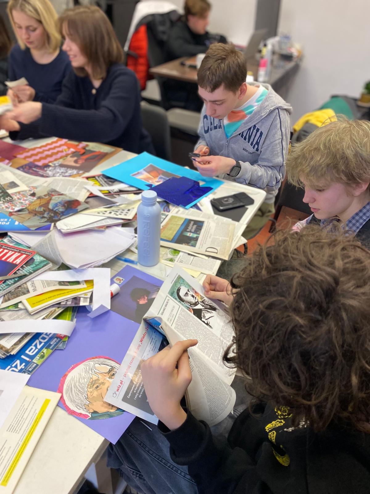 Uczniowie pracują przy stole pełnym magazynów i gazet, tworząc kolaże lub projekty artystyczne z wyciętymi materiałami.