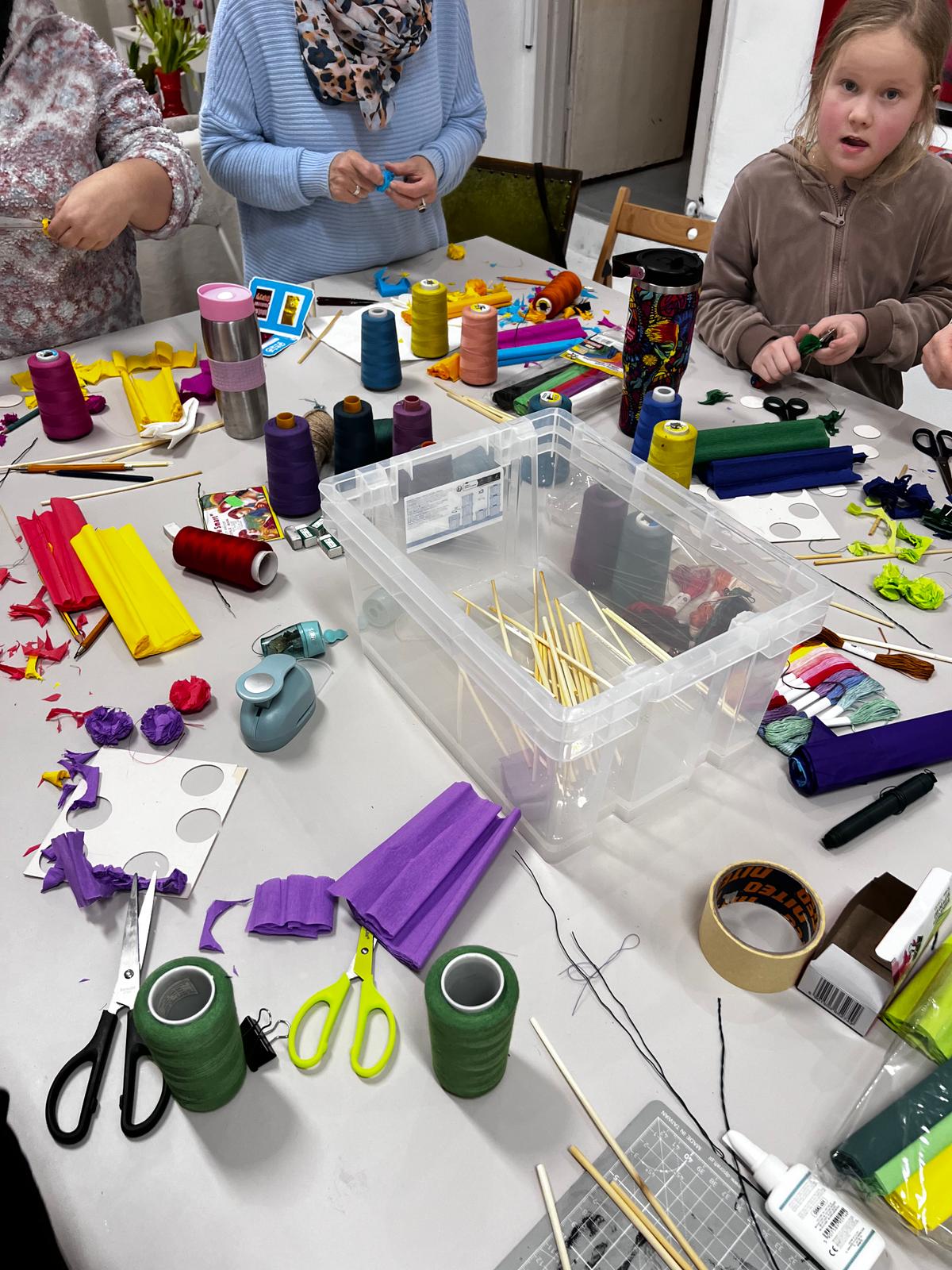 Dzieci uczestniczą w warsztatach rękodzieła, wykonując projekty z kolorowych nitek, taśm i różnych materiałów plastycznych.