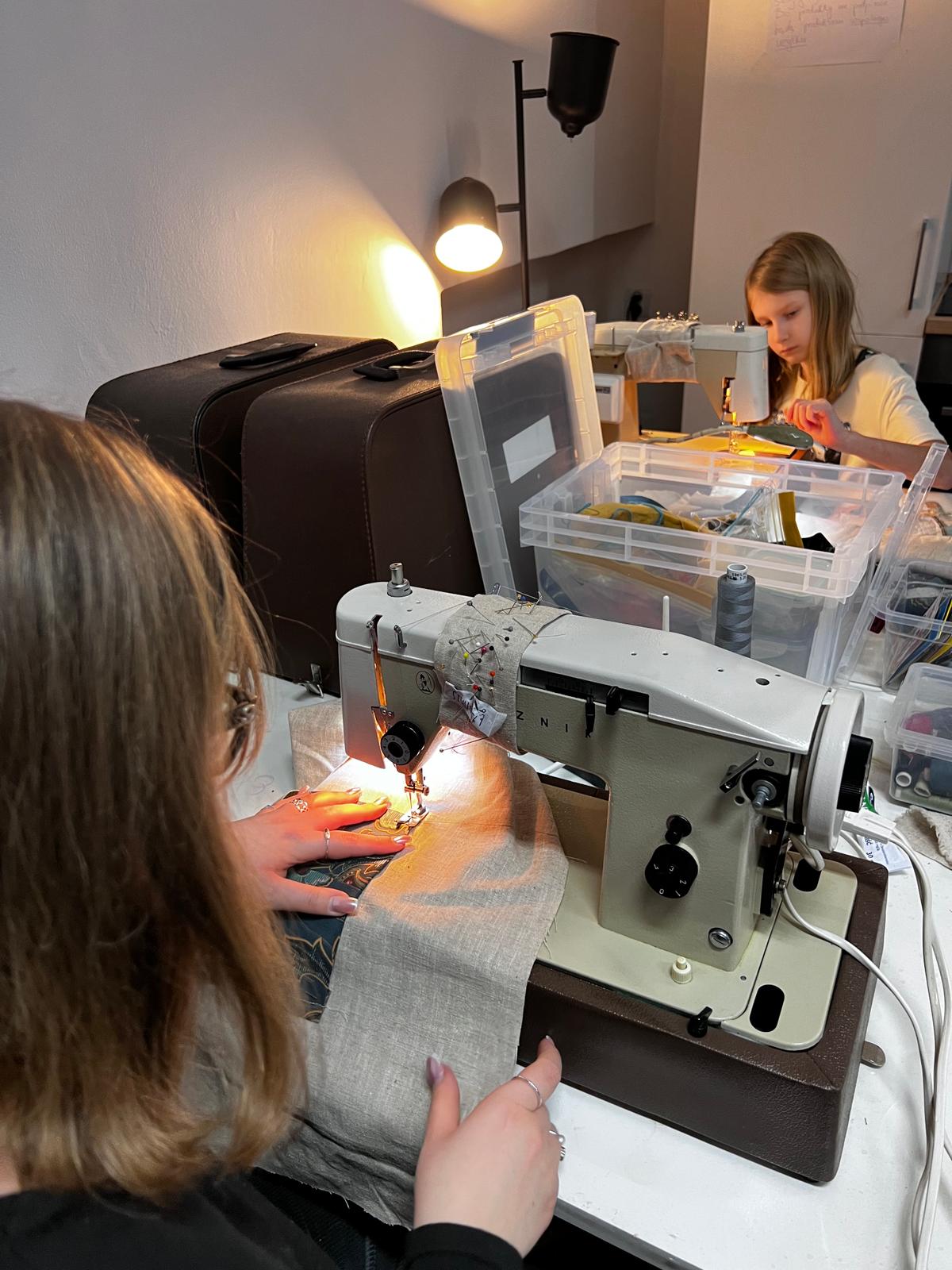 Dwie dziewczyny zajmują się szyciem na maszynach do szycia w jasno oświetlonej pracowni rzemieślniczej.