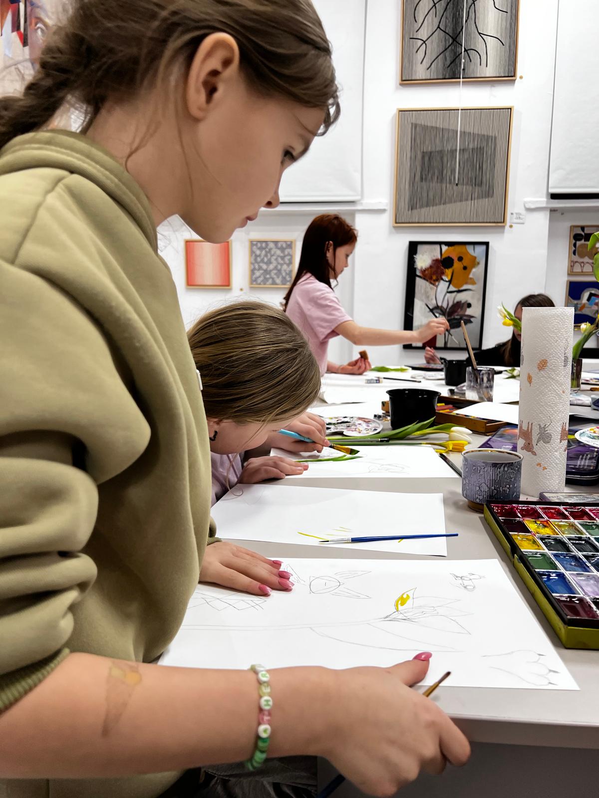 Dziewczyny uczestniczą w warsztacie artystycznym, rysując i malując przy stole pełnym materiałów do twórczości.