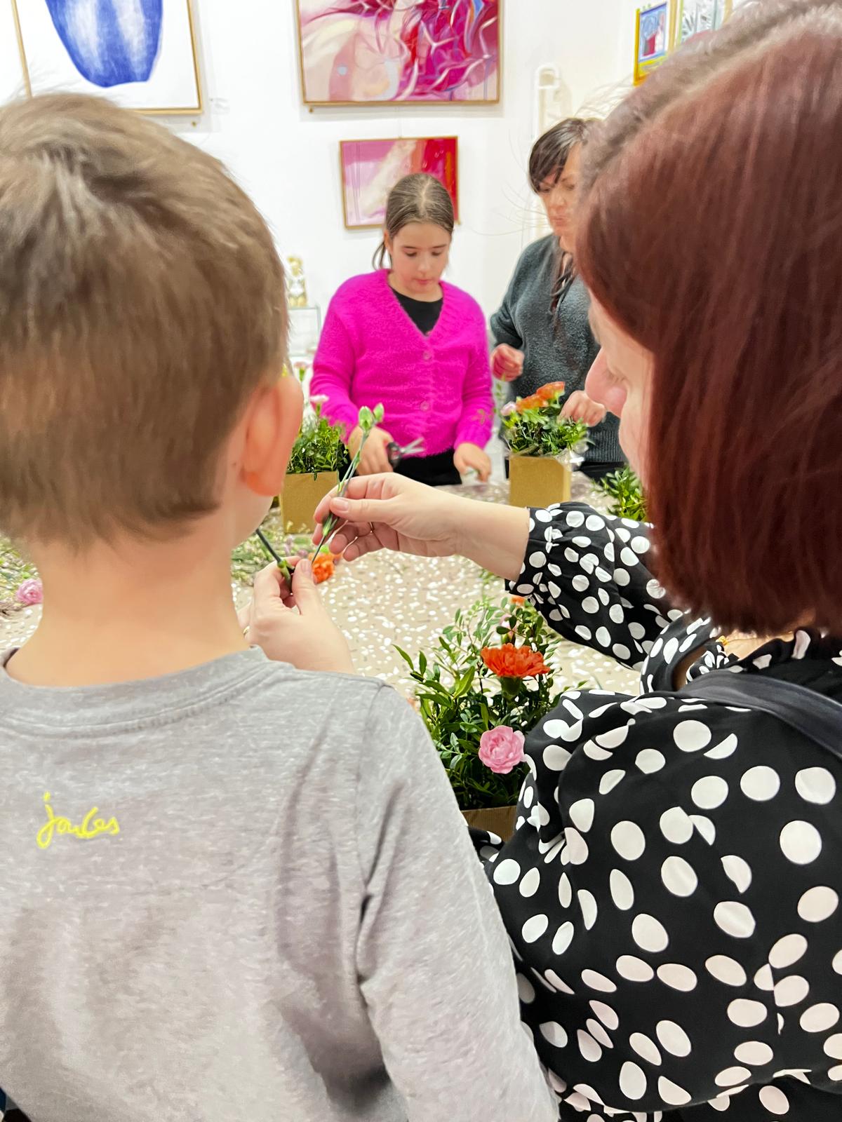 Dzieci uczestniczą w warsztatach florystycznych, układając kwiaty w doniczkach w klasie szkolnej.