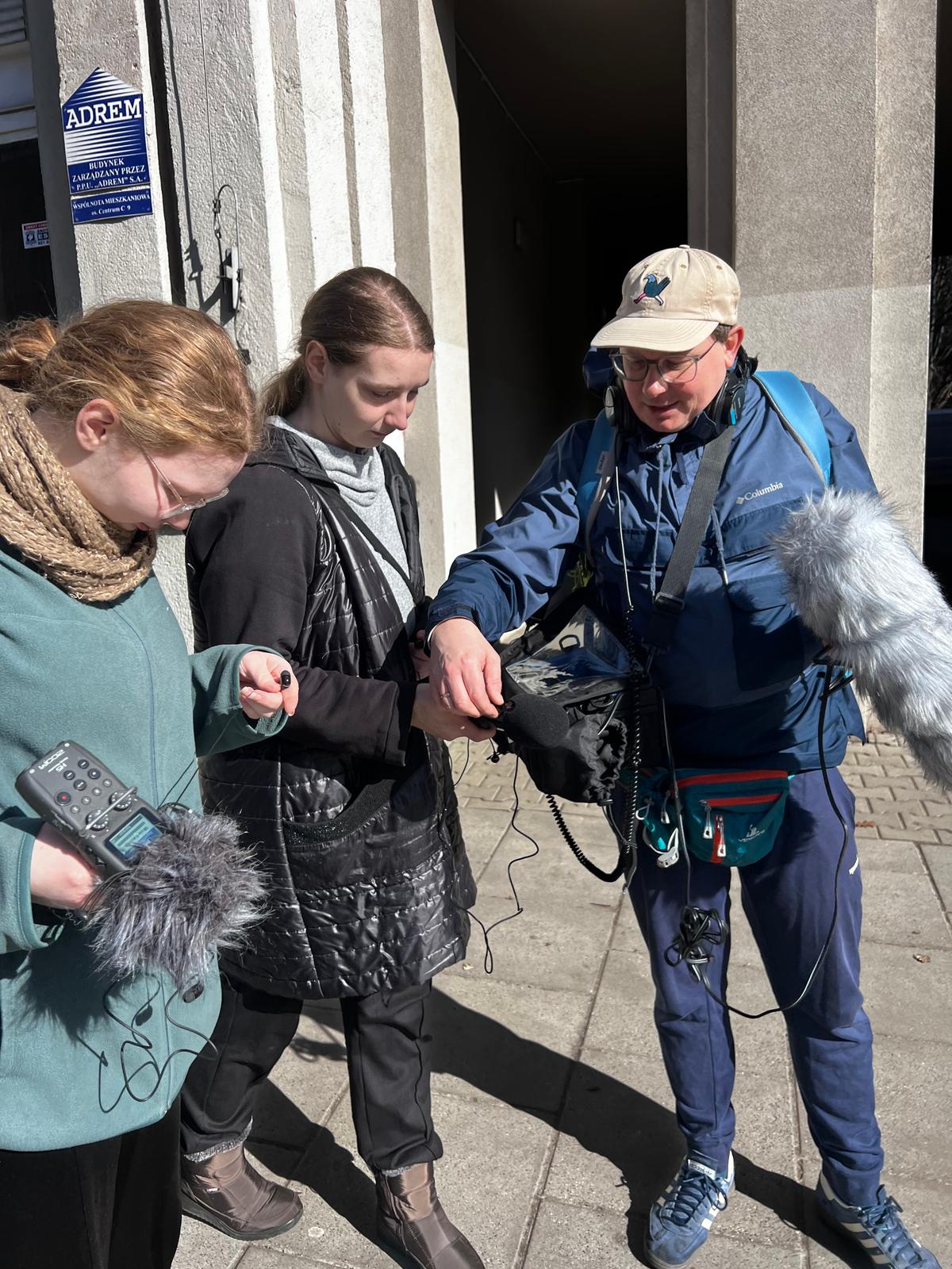 Troje ludzi przeprowadza rozmowę na ulicy, kobieta trzyma mikrofonofon i urządzenie do nagrywania dźwięku.