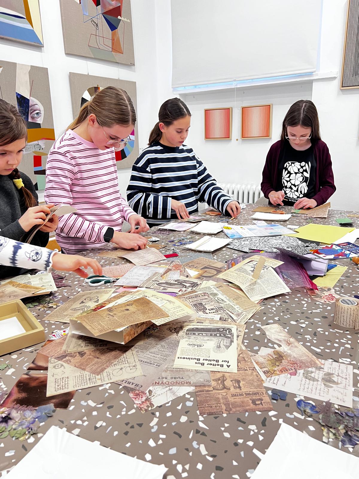 Cztery dziewczyny pracują przy stole, tworząc kolaż z recyklingu przy użyciu starych gazet i czasopism.