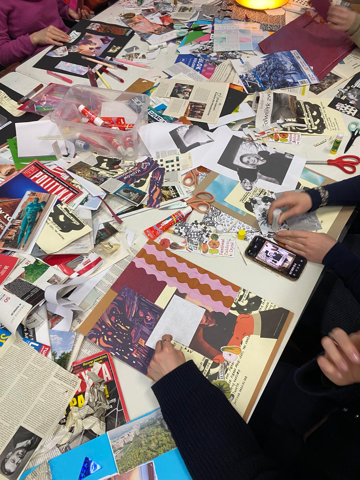 Grupa osób tworzy kolaż na stole, wykorzystując zdjęcia, magazyny, artykuły i różne materiały artystyczne.