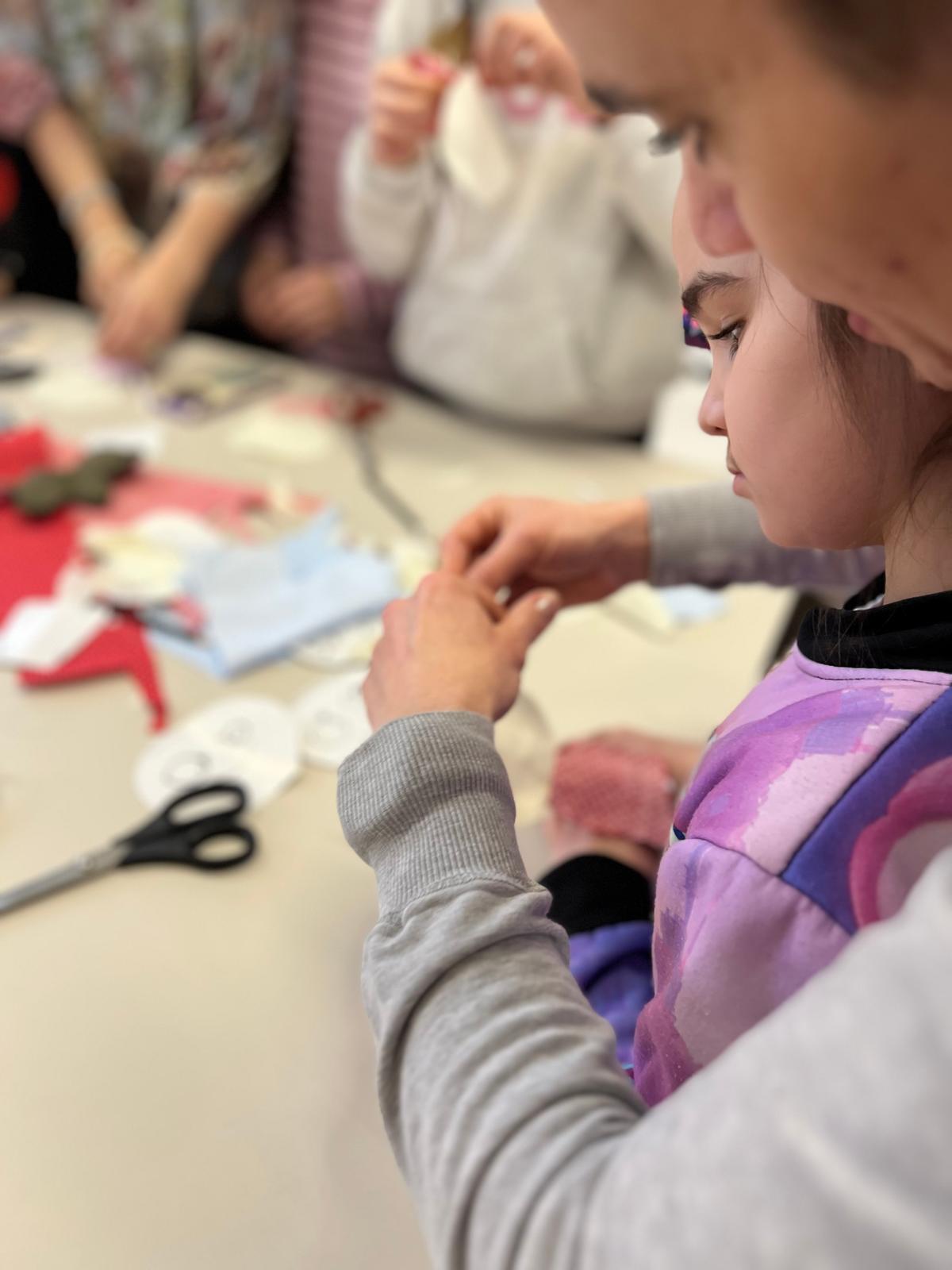 Dziewczynka w fioletowej kurtce zajęta pracą plastyczną podczas warsztatów twórczych z innymi dziećmi.