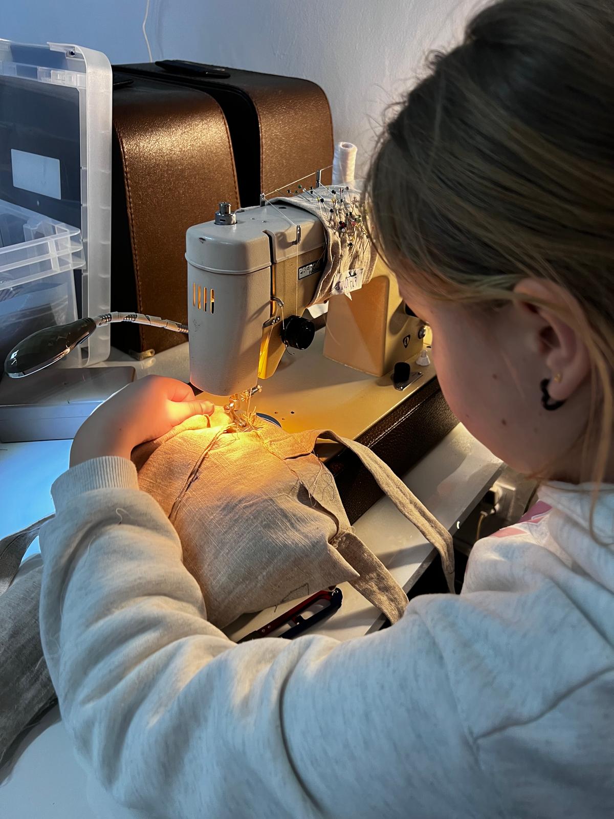 Kobieta pracuje na maszynie do szycia, przygotowując materiał do wykonania szydełka lub haftowania.