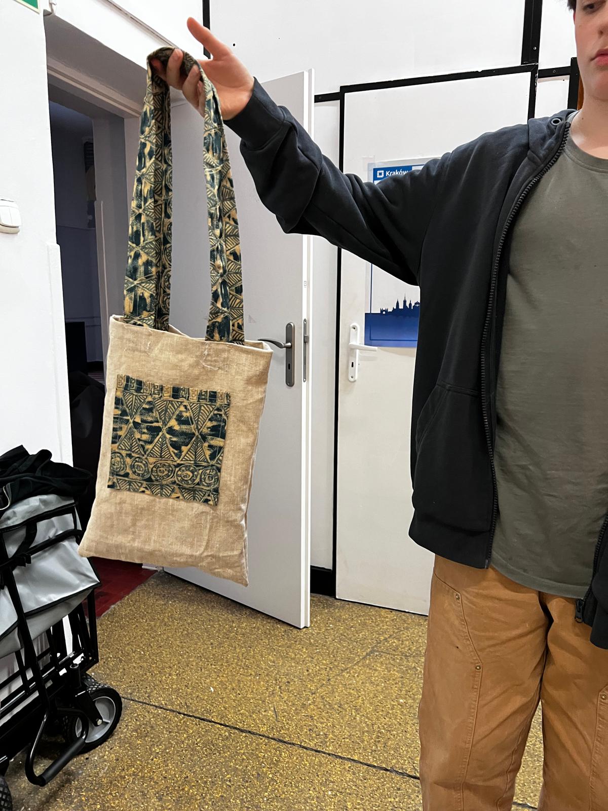 Mężczyzna prezentuje płóciną torbę z tradycyjnym czarno-złotym wzorem, trzymając ją za zawieszki.
