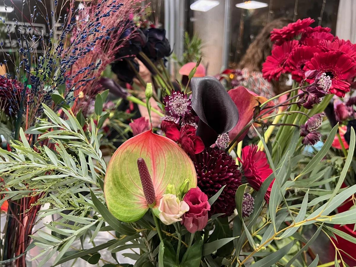 Bukiet kwiatów w odcieniach czerwieni i różu z anthurium, gerberami i ozdobną zielenią na wystawie florystycznej.