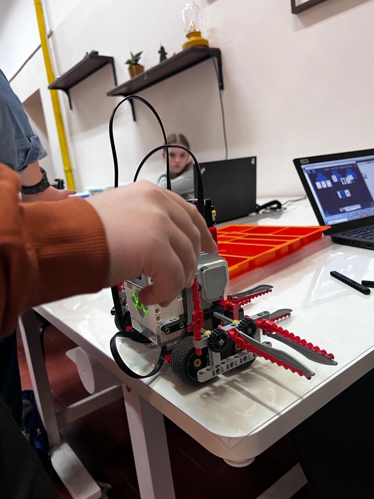 Osoba pracuje nad robotycznym urządzeniem w kolorze czerwonym podczas zajęć edukacyjnych w pracowni.