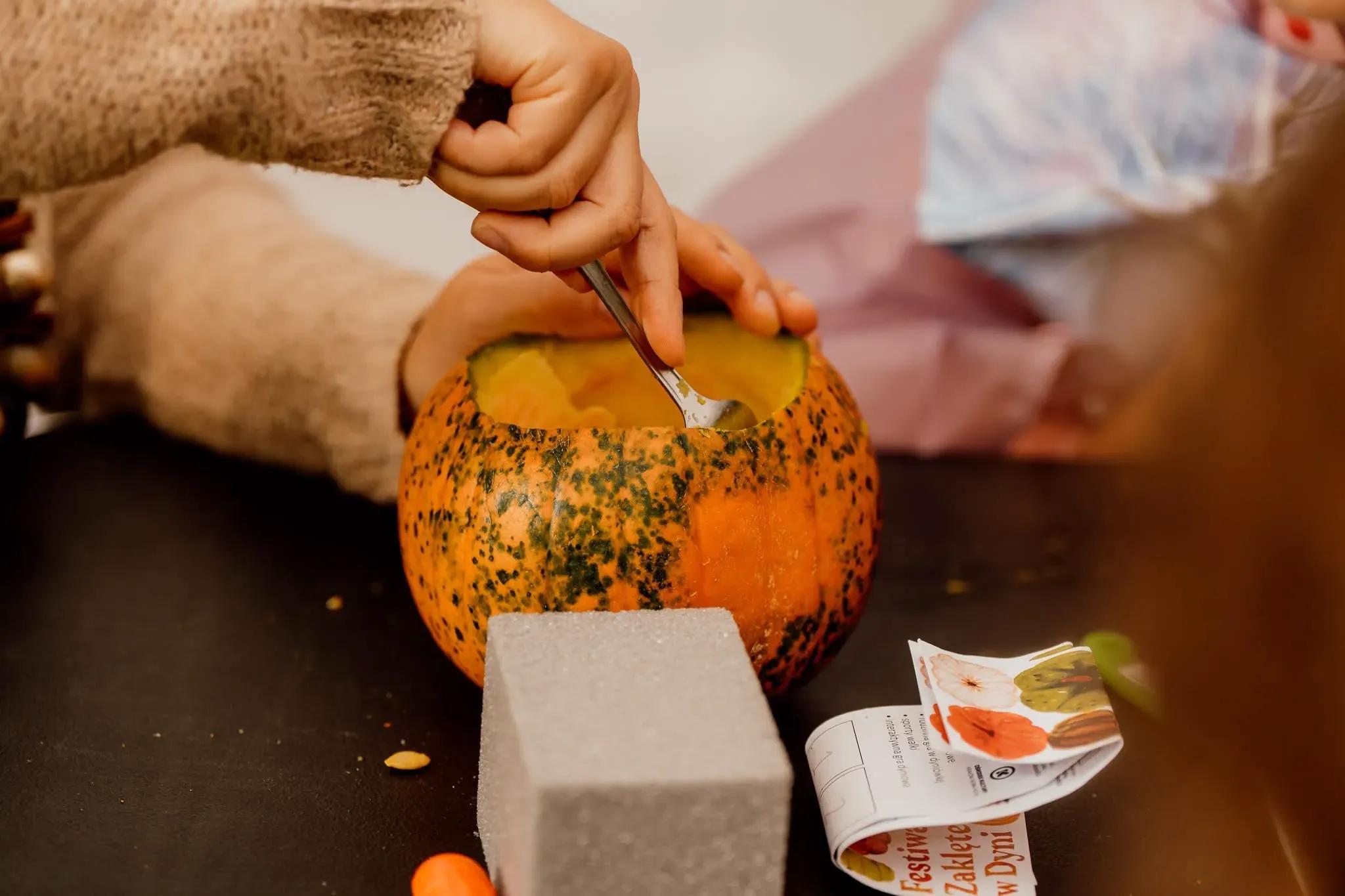 Dziecko wyskrobuje nasiona z pomarańczowej dyni, a obok leży instrukcja sadzonka.