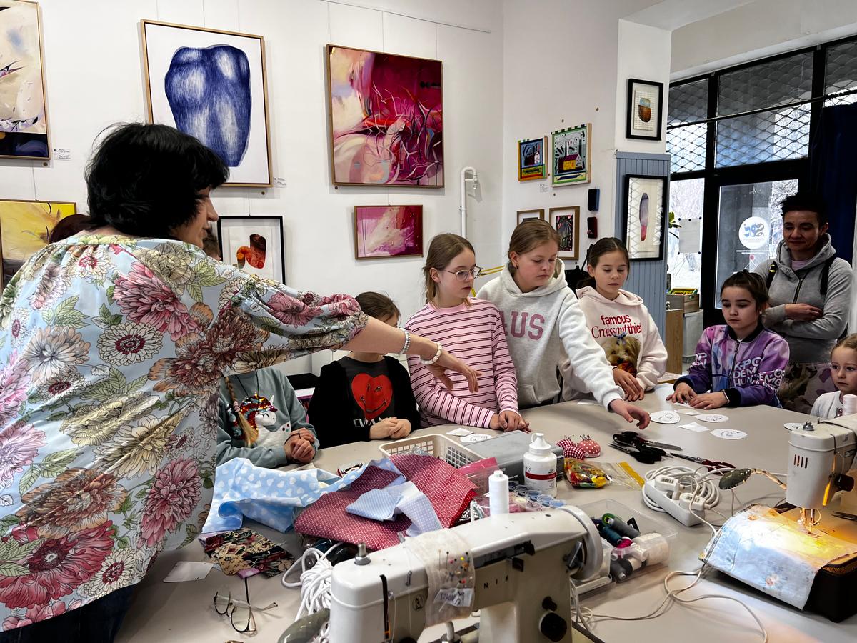 Instruktorka prowadzi warsztat krawiecki dla grupy dzieci w studio sztuki, gdzie uczą się szycia przy maszynach.