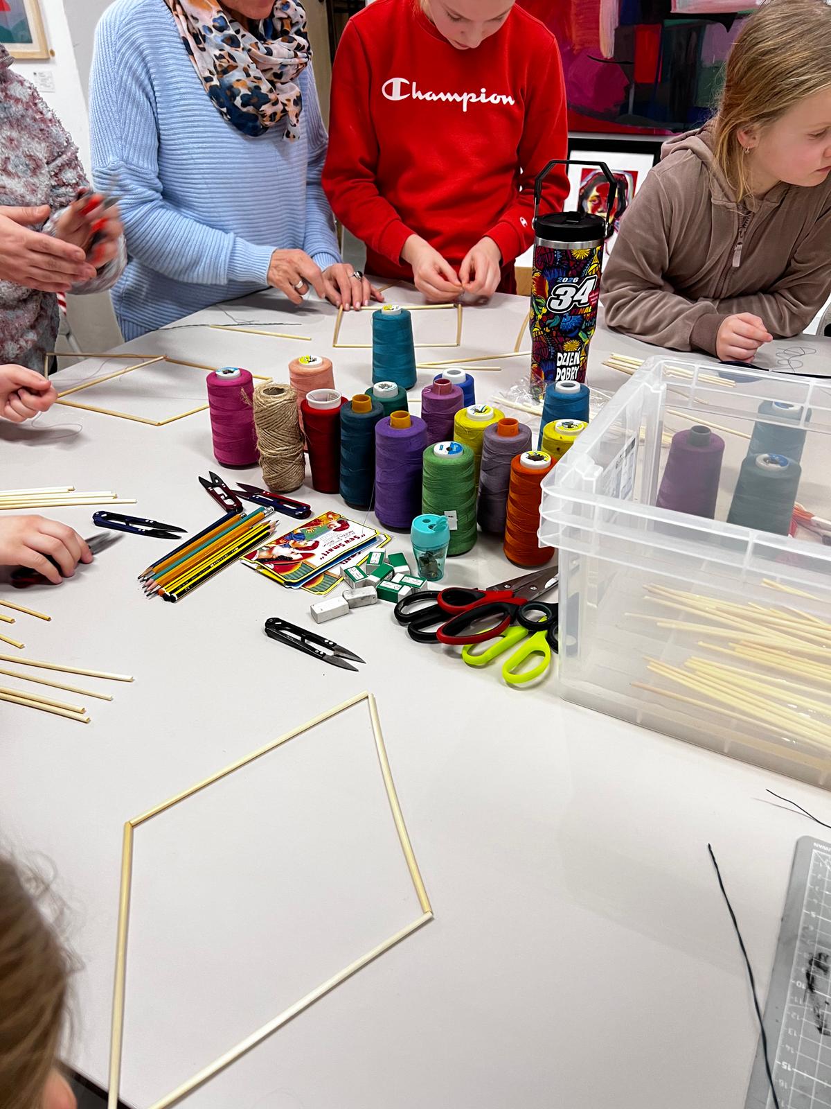 Dzieci uczestniczą w warsztacie kreatywnym, wyplatając kolorowe sznurki przy stole z materiałami artystycznymi.