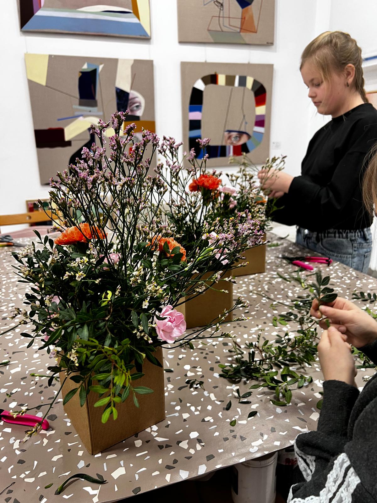 Dziewczyna układa bukiet kwiatów w pudełku podczas warsztatu florystycznego w galerii sztuki.