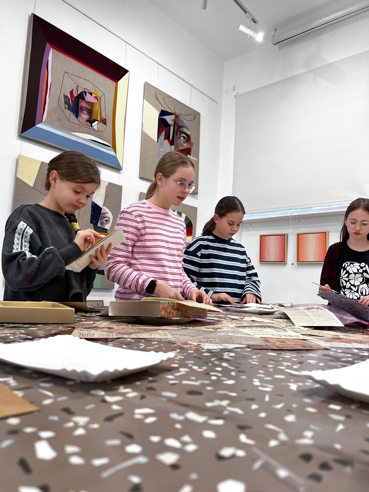 Dziewczyny oglądają wystawę sztuki współczesnej w galerii, przeglądając materiały edukacyjne na stole.
