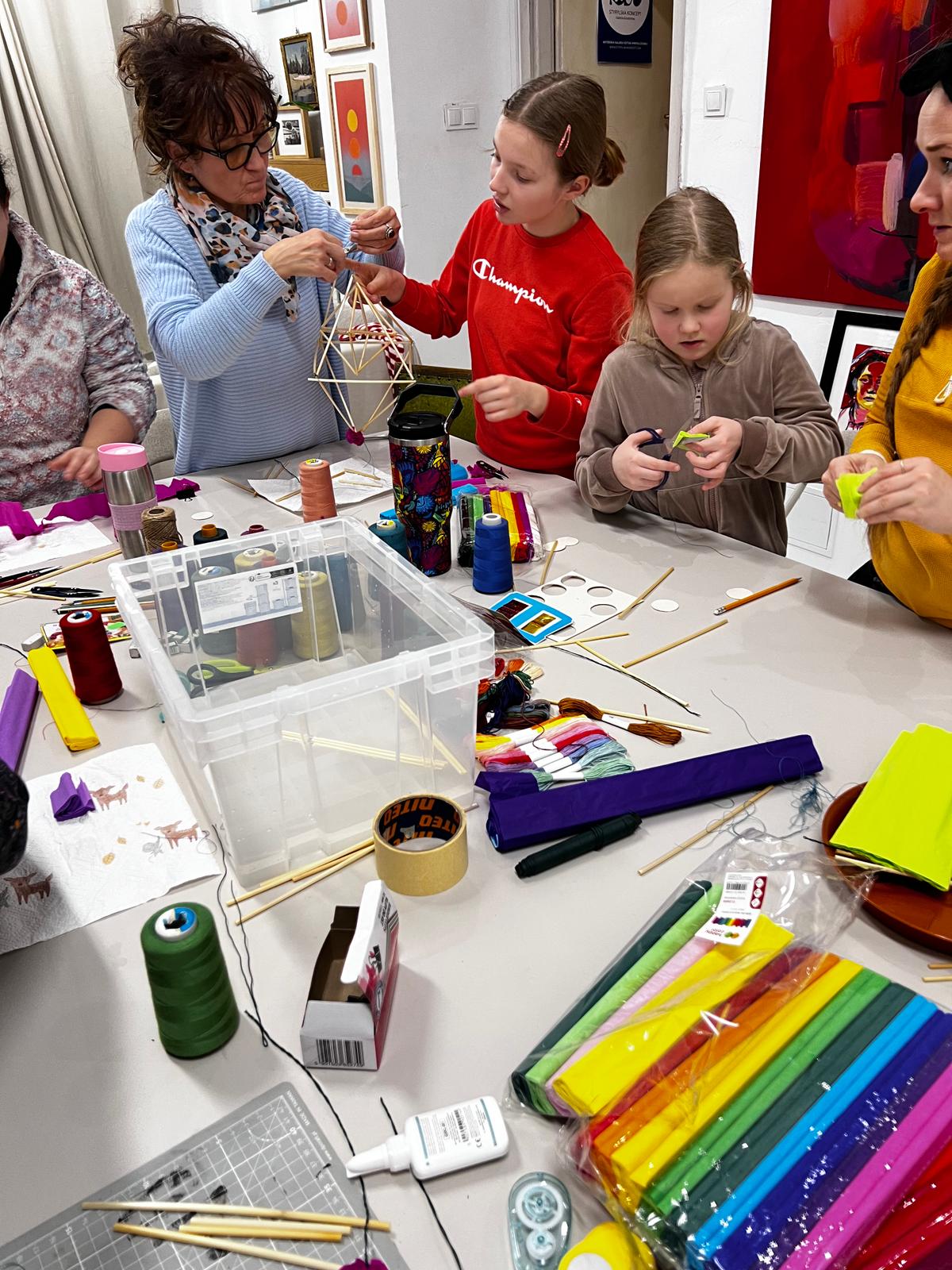 Kobieta i dzieci uczestniczą w warsztacie twórczym, pracując z kolorowymi materiałami rzemieślniczymi na stole.