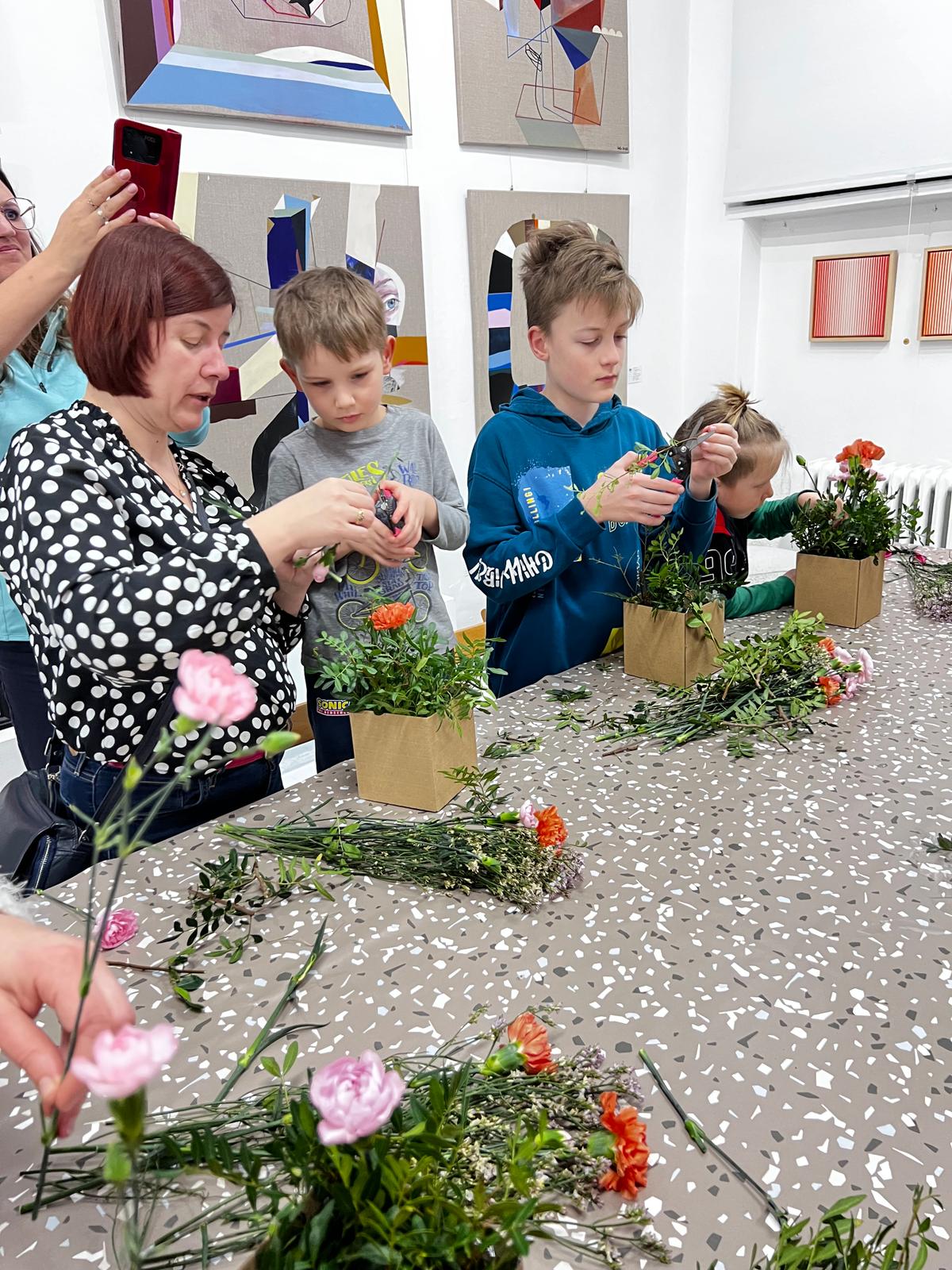 Kobieta i dzieci wspólnie przesadzają kolorowe kwiaty do doniczek w galerii sztuki.