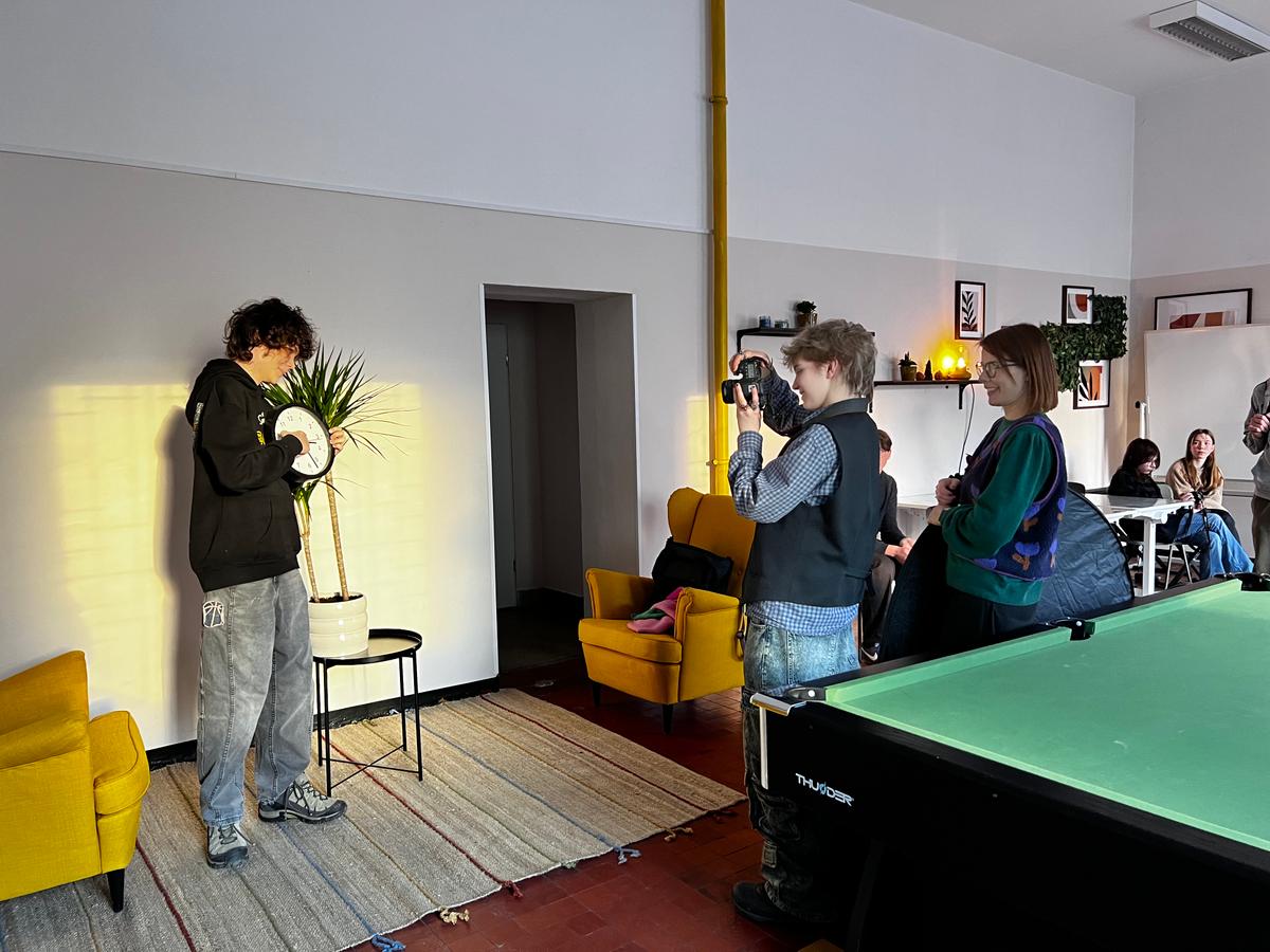 W nowoczesnym salonie grupa młodych osób pozuje do zdjęcia przy stole do ping-ponga, oświetlonym żółtym światłem.