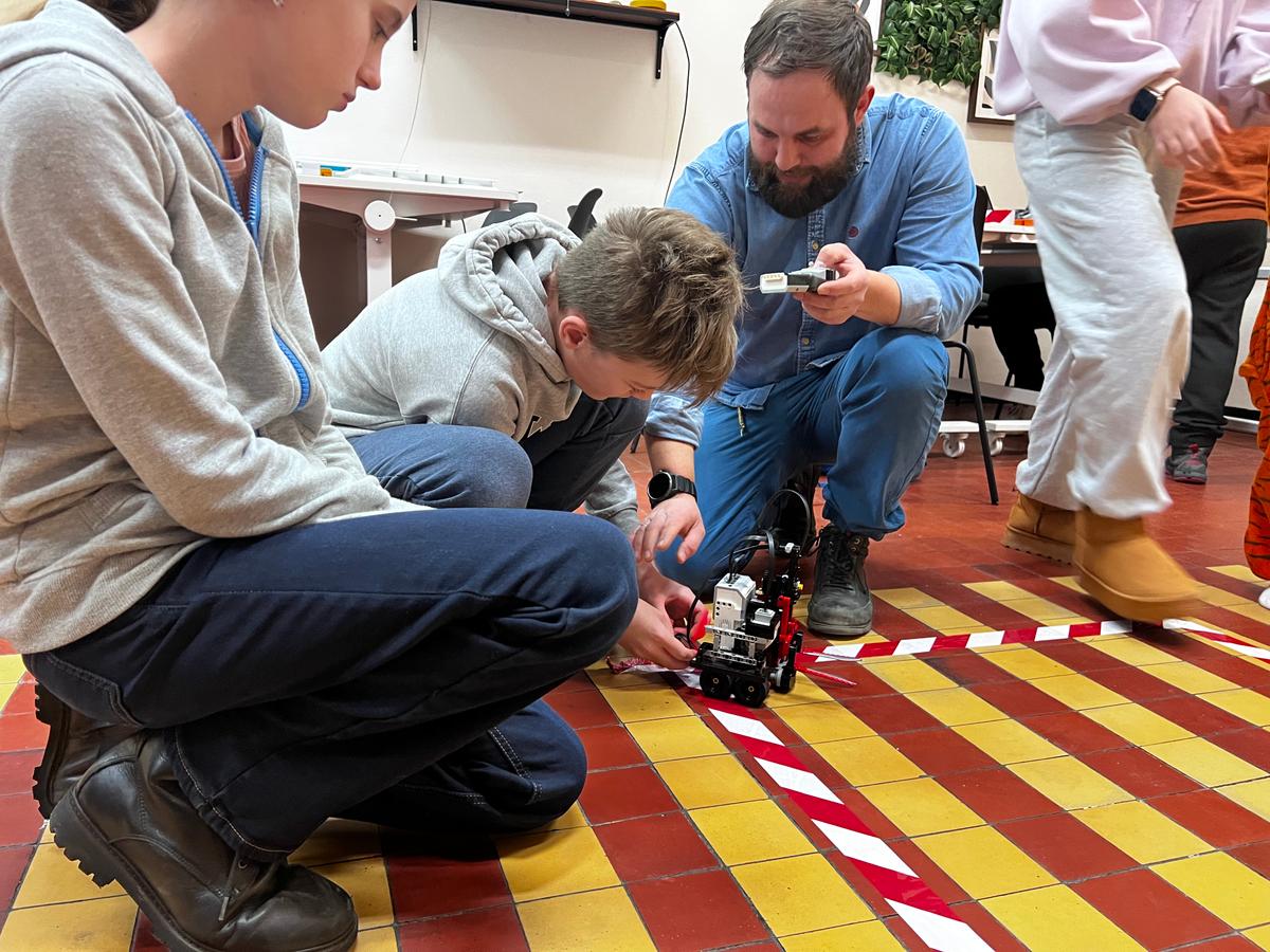 Nauczyciel demonstruje uczniom robota na podłodze w klasie podczas lekcji robotyki.