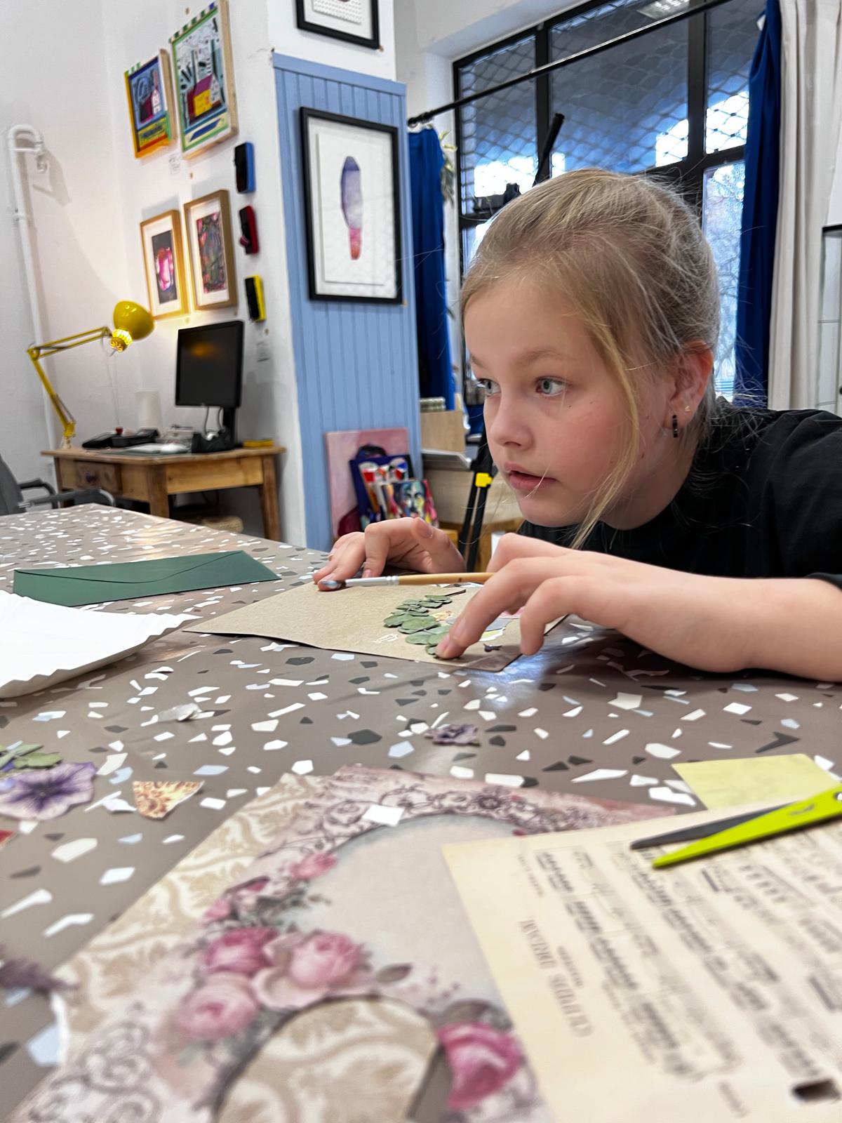 Dziewczyna pracuje nad projektem artystycznym przy stole, otoczona materiałami kreatywymi w nowoczesnym studio.