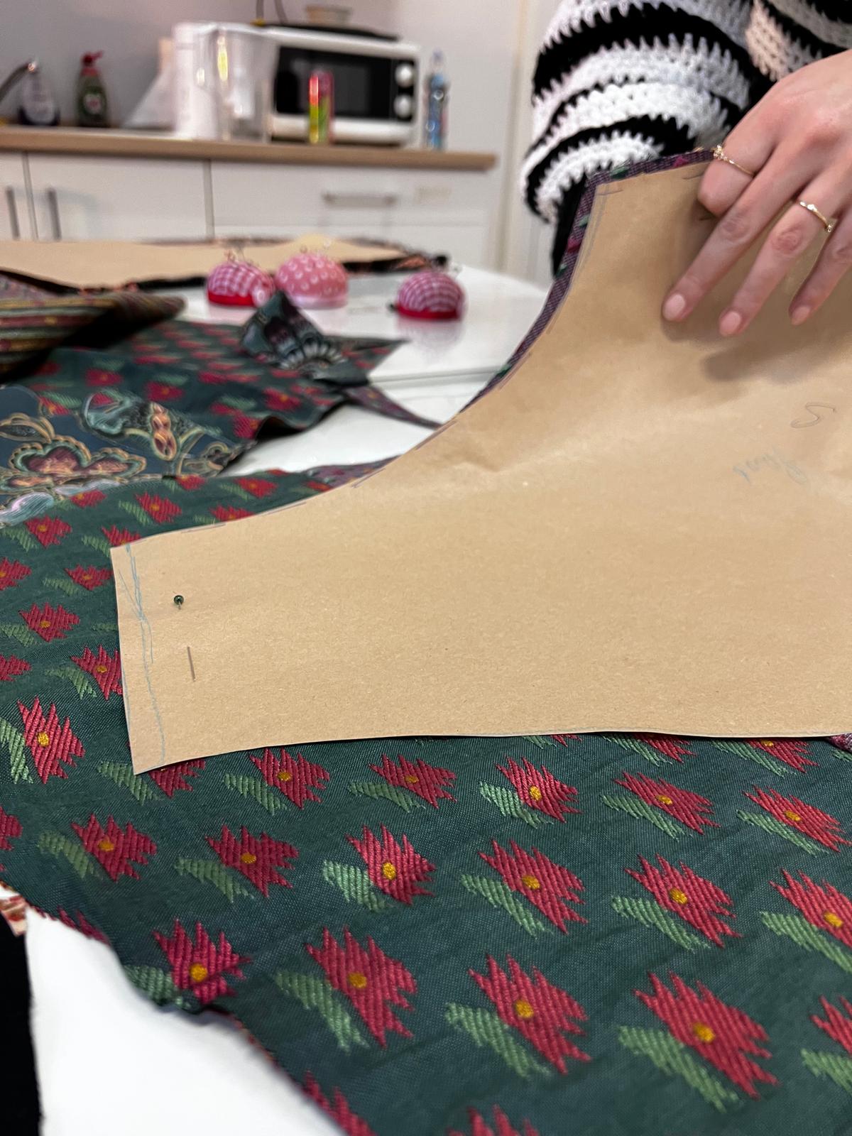 Kobieta pracuje nad projektem krawiectwa, szyując tkaninę w kuchni obok narzędzi krawieckich.