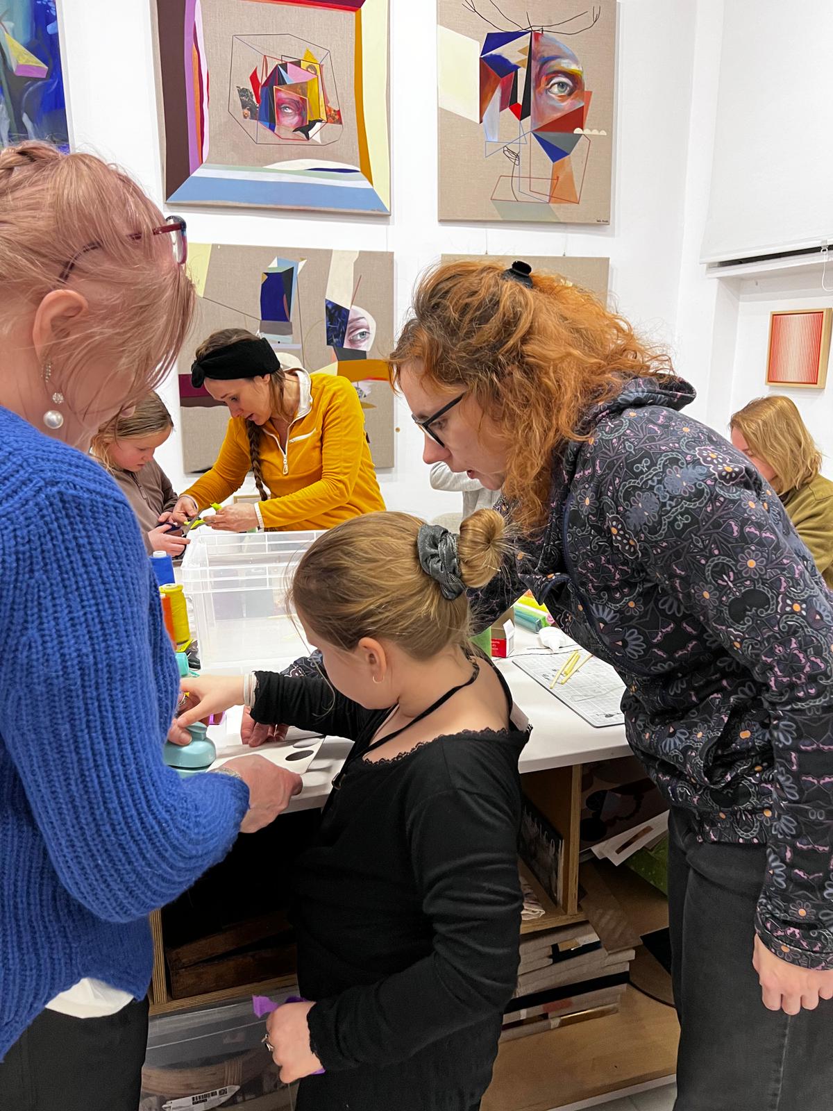 Grupa osób uczestniczy w warsztacie artystycznym w galerii, gdzie instruktorka w żółtej kurtce pokazuje uczestnikom technikę rysowania.