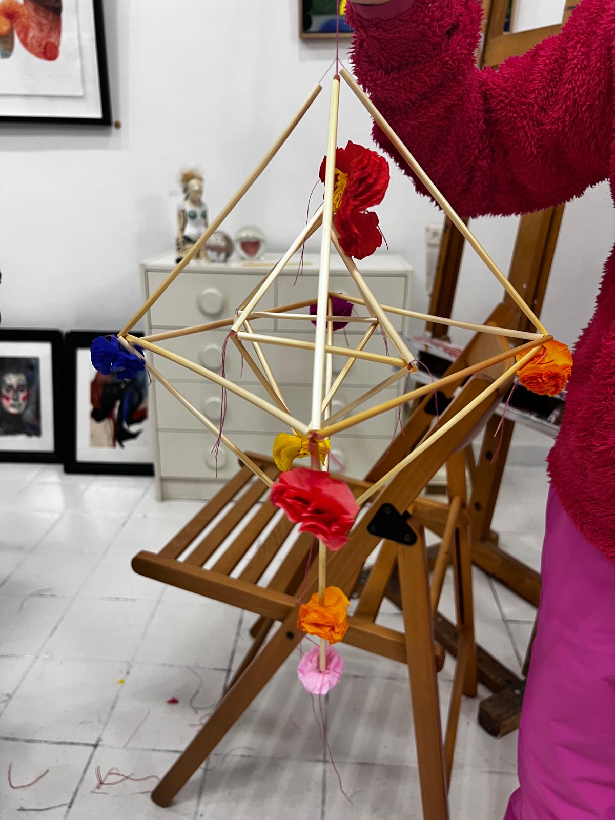 Drewniana gwiazda z zawieszonym kwiatami w różnych kolorach stoi na drewnianym stojaku w galerii sztuki.