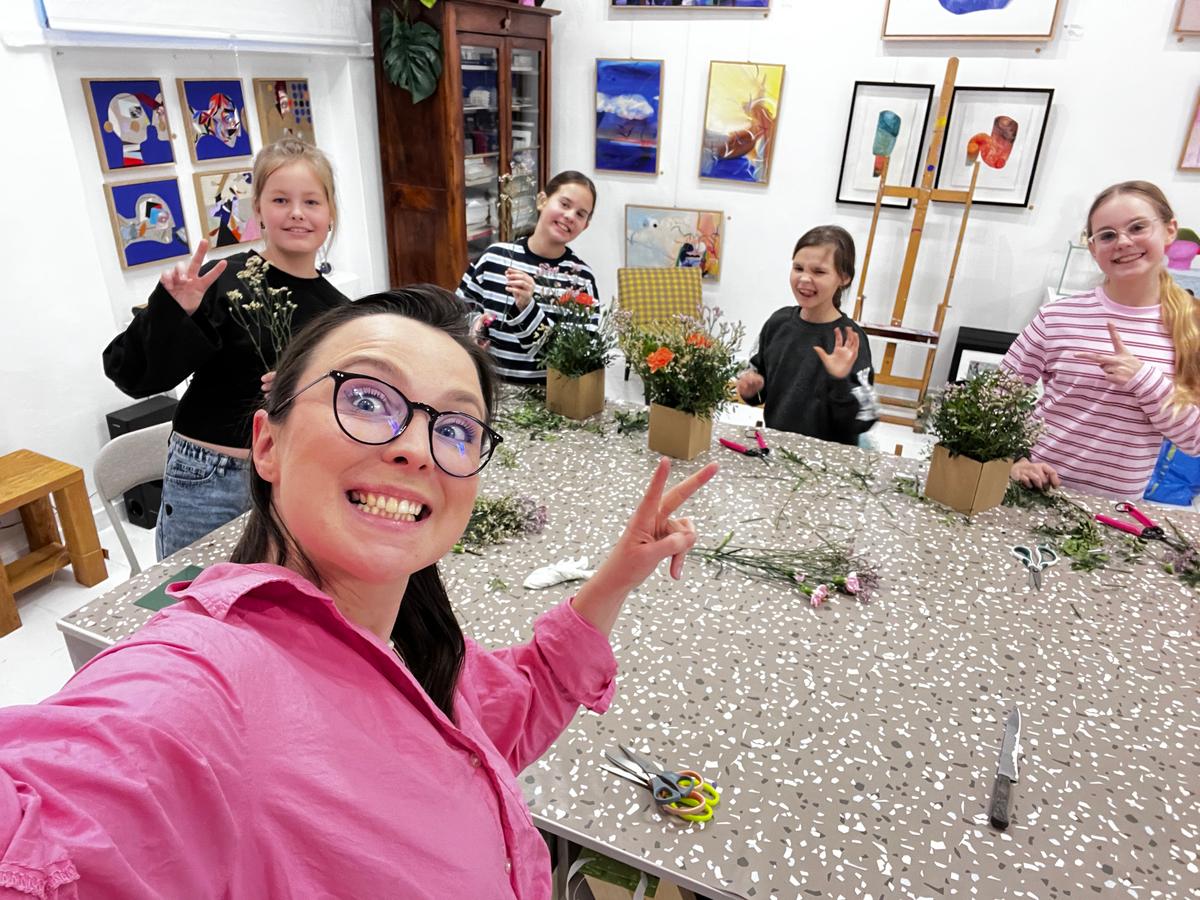 Grupa radosnych dziewczyn w pracowni artystycznej podczas zajęć twórczych z kwiatami i materiałami do rękodzieła.