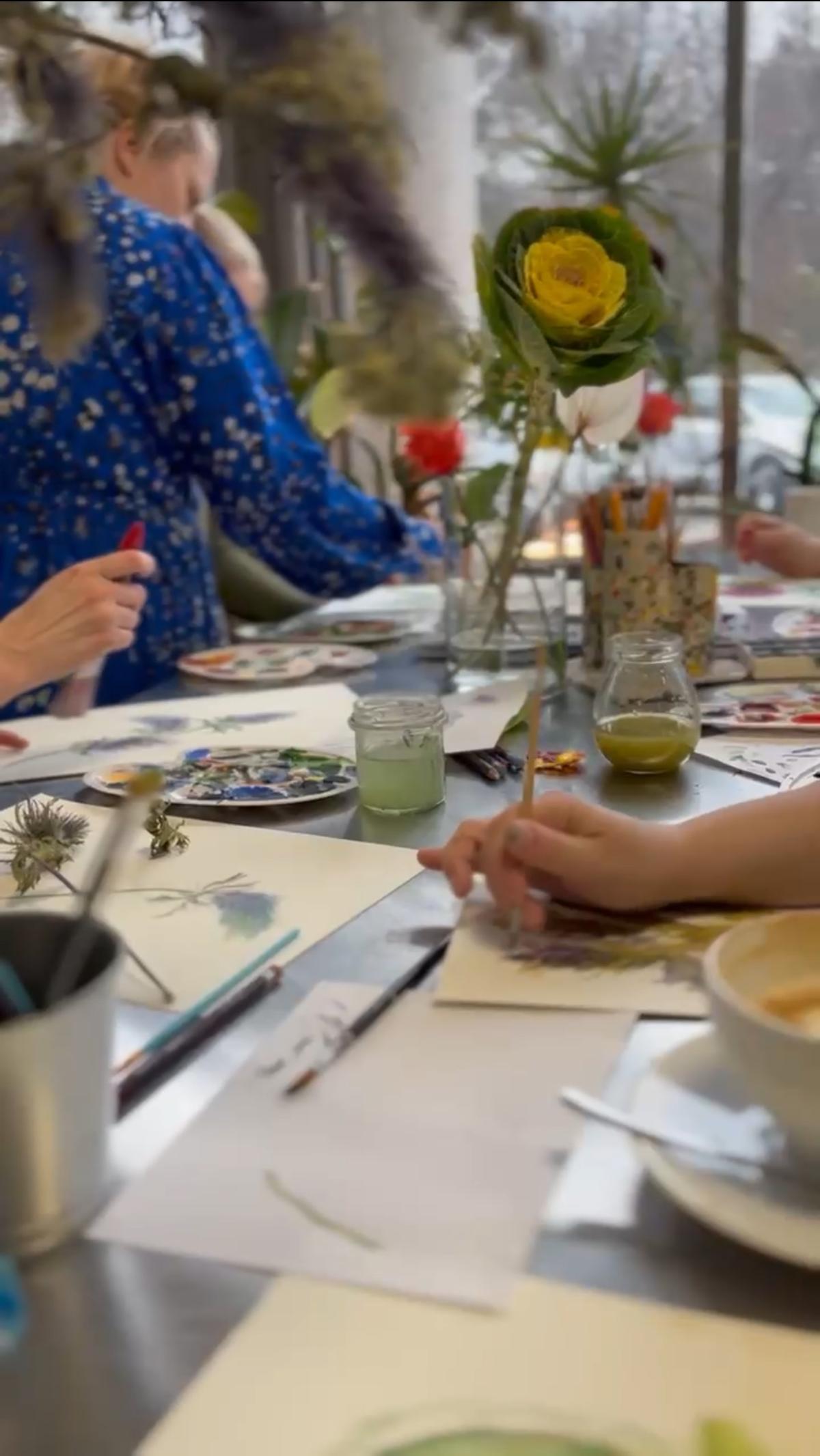 Dzieci uczestniczą w warsztatach artystycznych przy stole, malując i rysując obok żywych kwiatów.