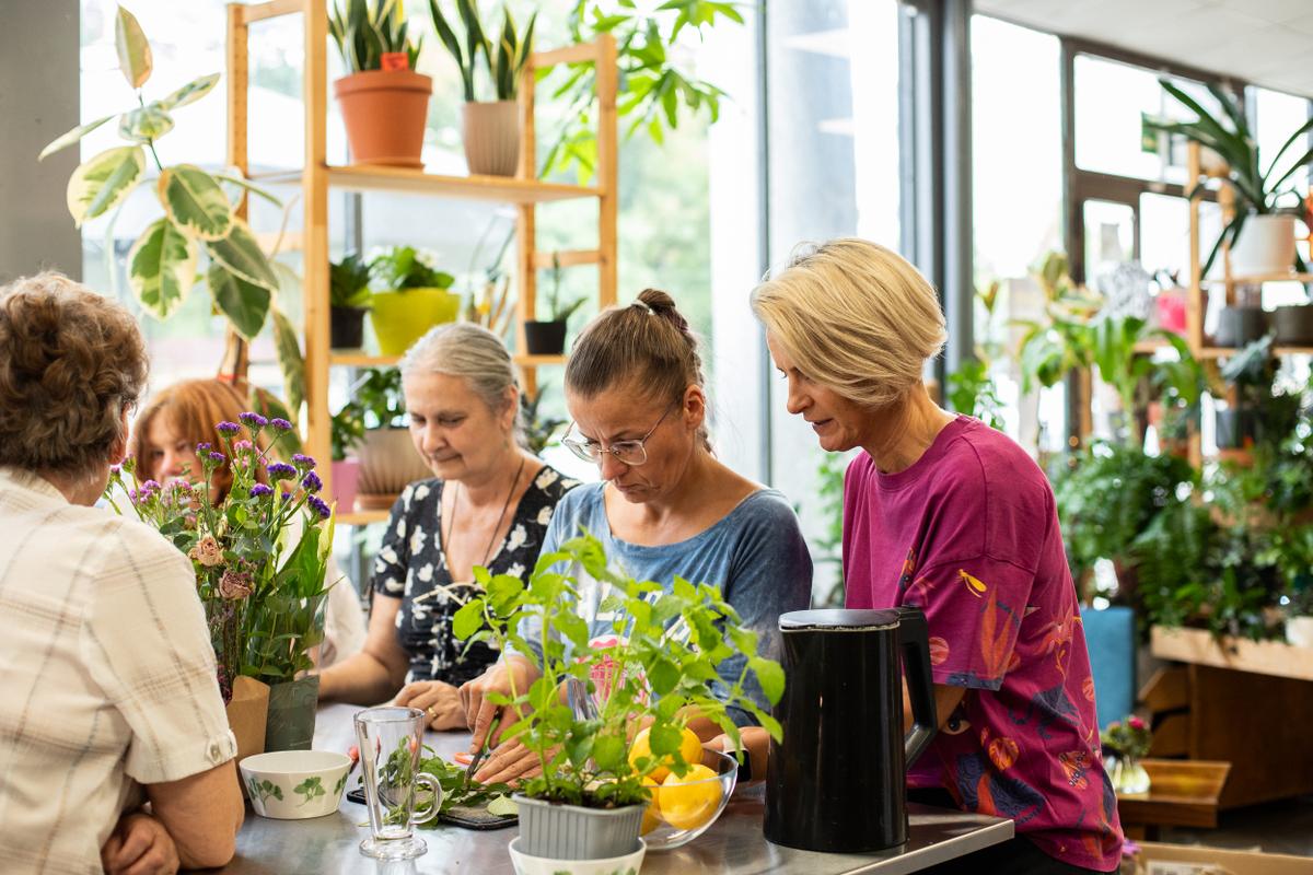 Grupa kobiet uczestniczy w warsztacie dotyczącym roślin doniczkowych w jasnym pomieszczeniu pełnym zieleni.