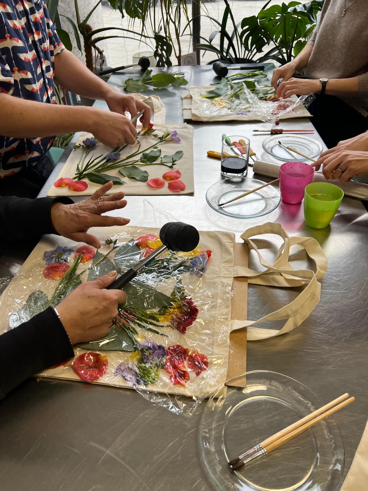 Grupa osób wykonuje wspólnie warsztat twórczy z kwiatami, przygotowując je do naciśnięcia i umieszczenia na materiałach.