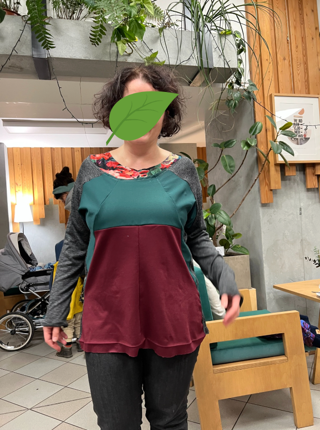 Kobieta w kolorowej bluzie stoi w nowoczesnym wnętrzu pełnym roślin doniczkowych.