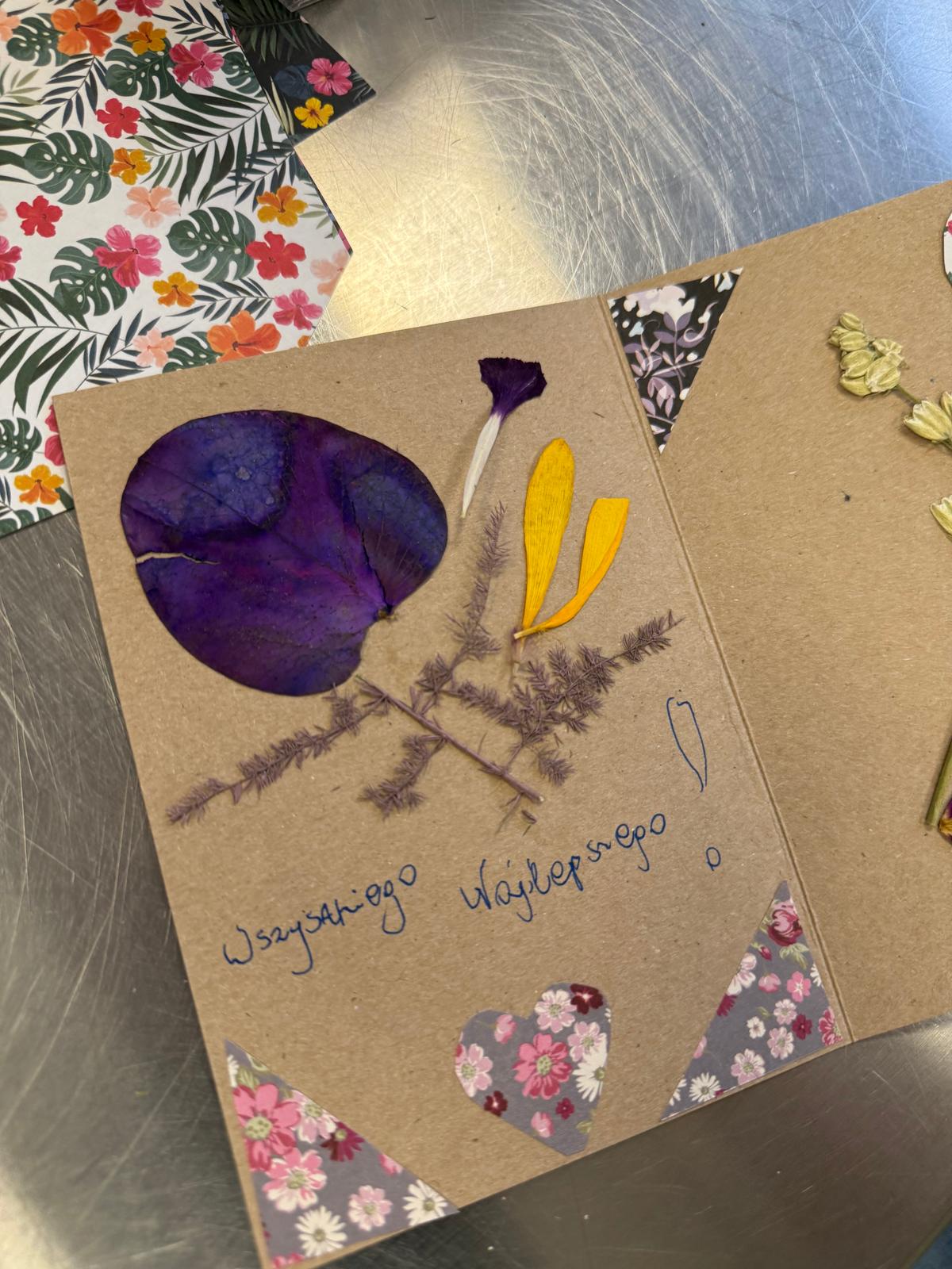 Kartka pamiątkowa z prasowanymi kwiatami: fioletowym płatkiem, żółtymi liśćmi i gałęzką.