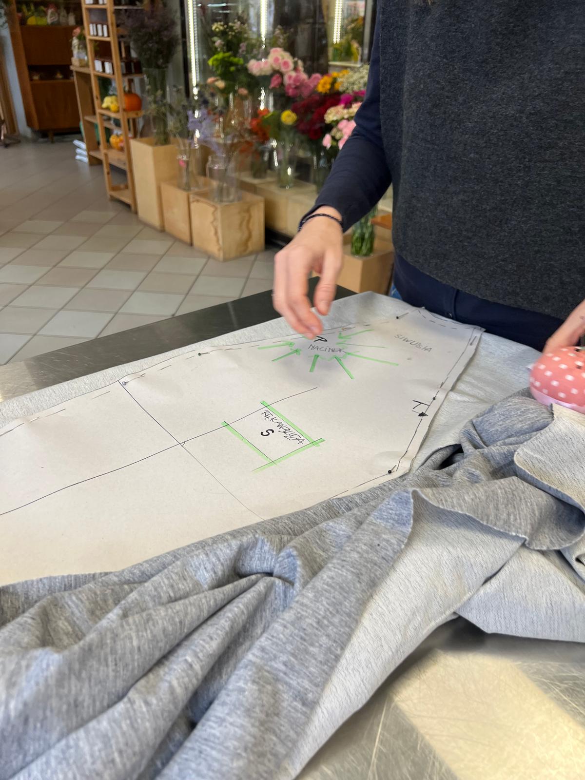 Osoba projektuje układ wnętrza na papierze, otoczona próbkami tkanin i kwiatami w kwiaciarni.