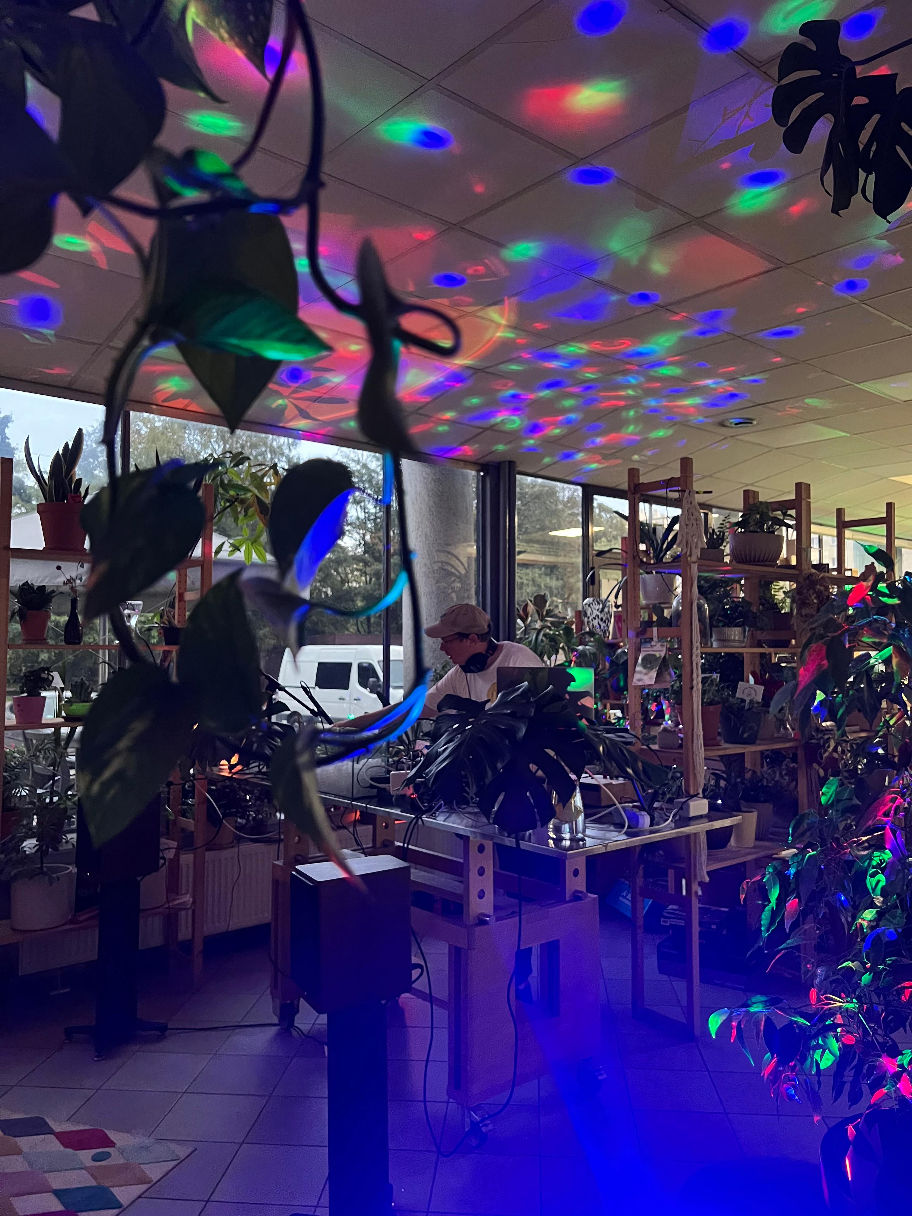 Mężczyzna pracuje przy biurku w nowoczesnym wnętrzu oświetlonym kolorowymi światłami LED, otoczonym roślinami.