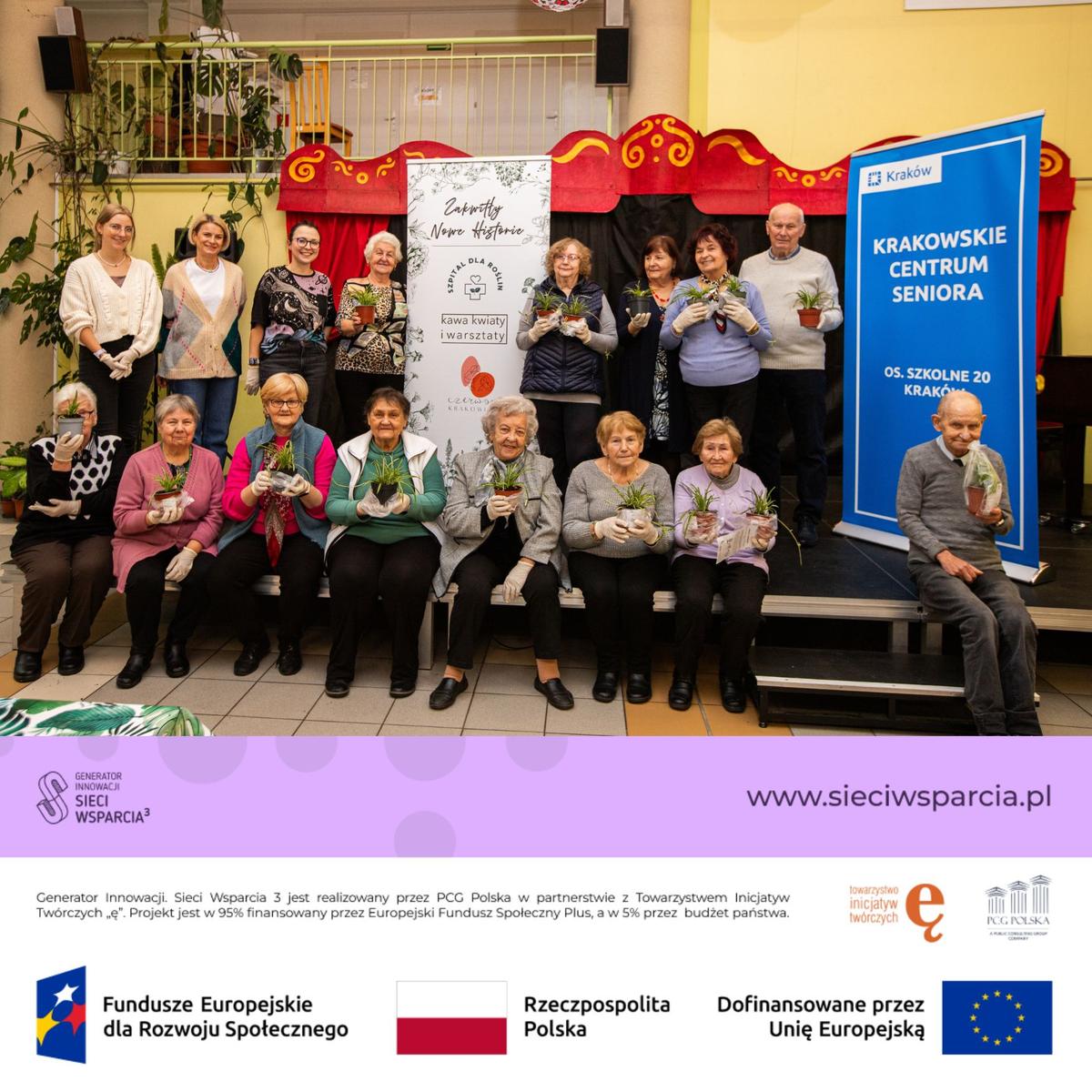 Grupa seniorów z Krakowskiego Centrum Seniora pozuje do zdjęcia trzymając rośliny podczas wydarzenia edukacyjnego.