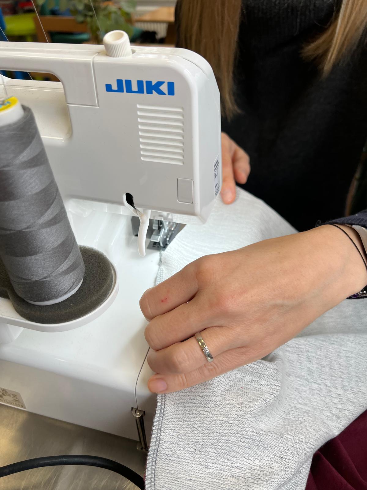 Osoba szyje białą tkaninę na maszynie do szycia marki Juki.