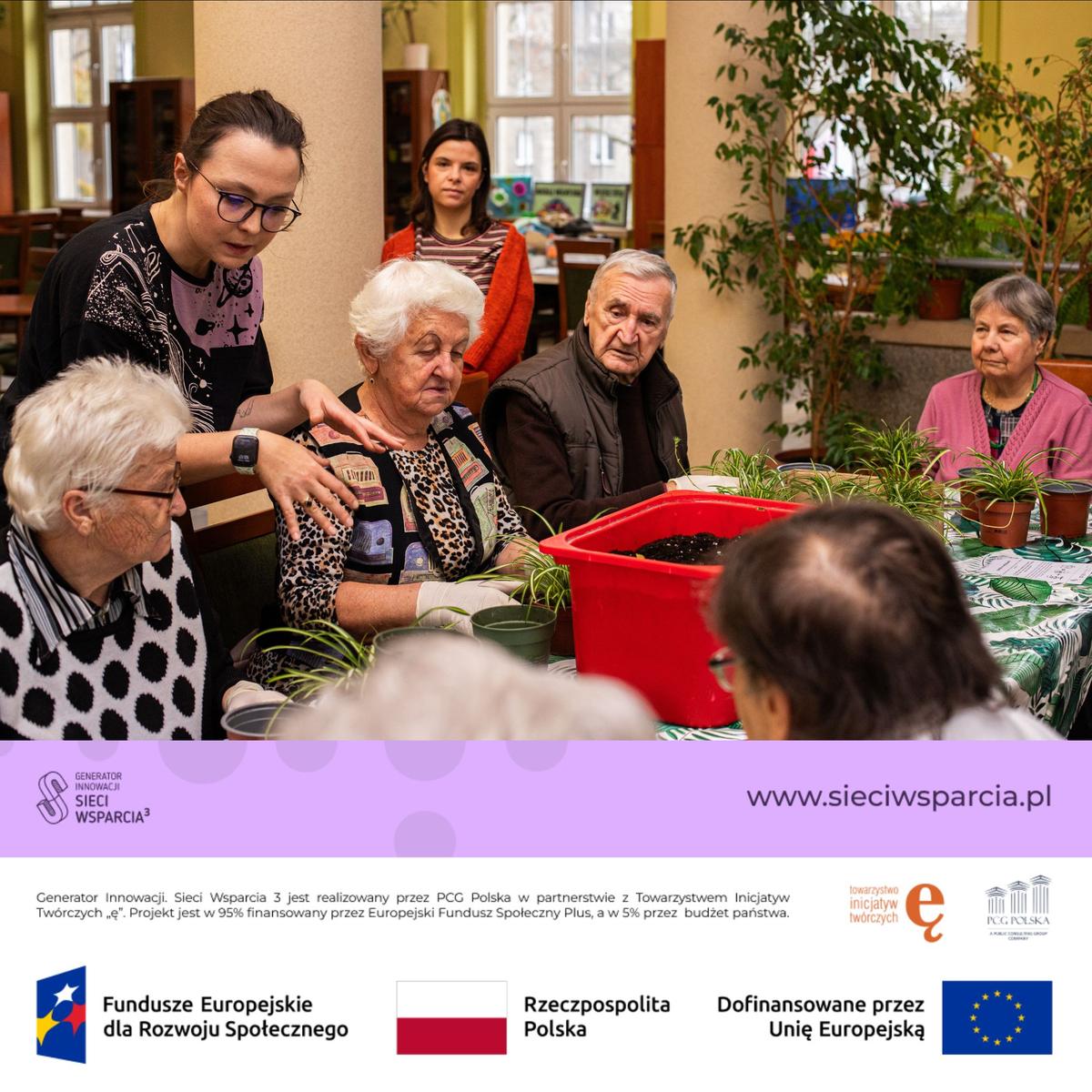 Intergeneracyjne spotkanie podczas warsztatów ogrodniczych, gdzie młoda kobieta uczy starszych uczestników sadzenia roślin.