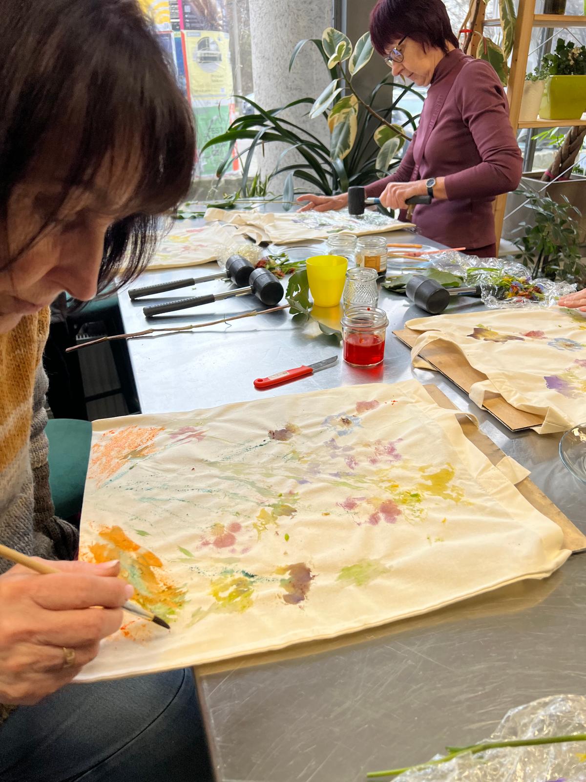 Kobieta podczas warsztatu botanicznego tworzy rysunek z użyciem suszonych kwiatów i roślin na papierze.