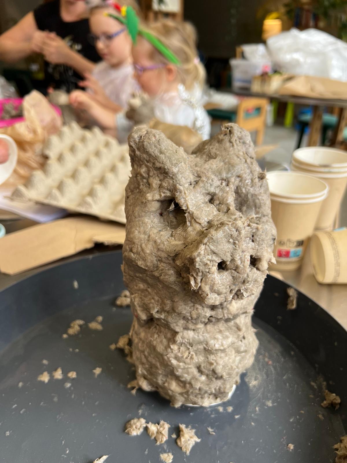 Dziecko modeluje figurkę zwierzęcia z szarego materiału podczas zajęć twórczych w grupie.