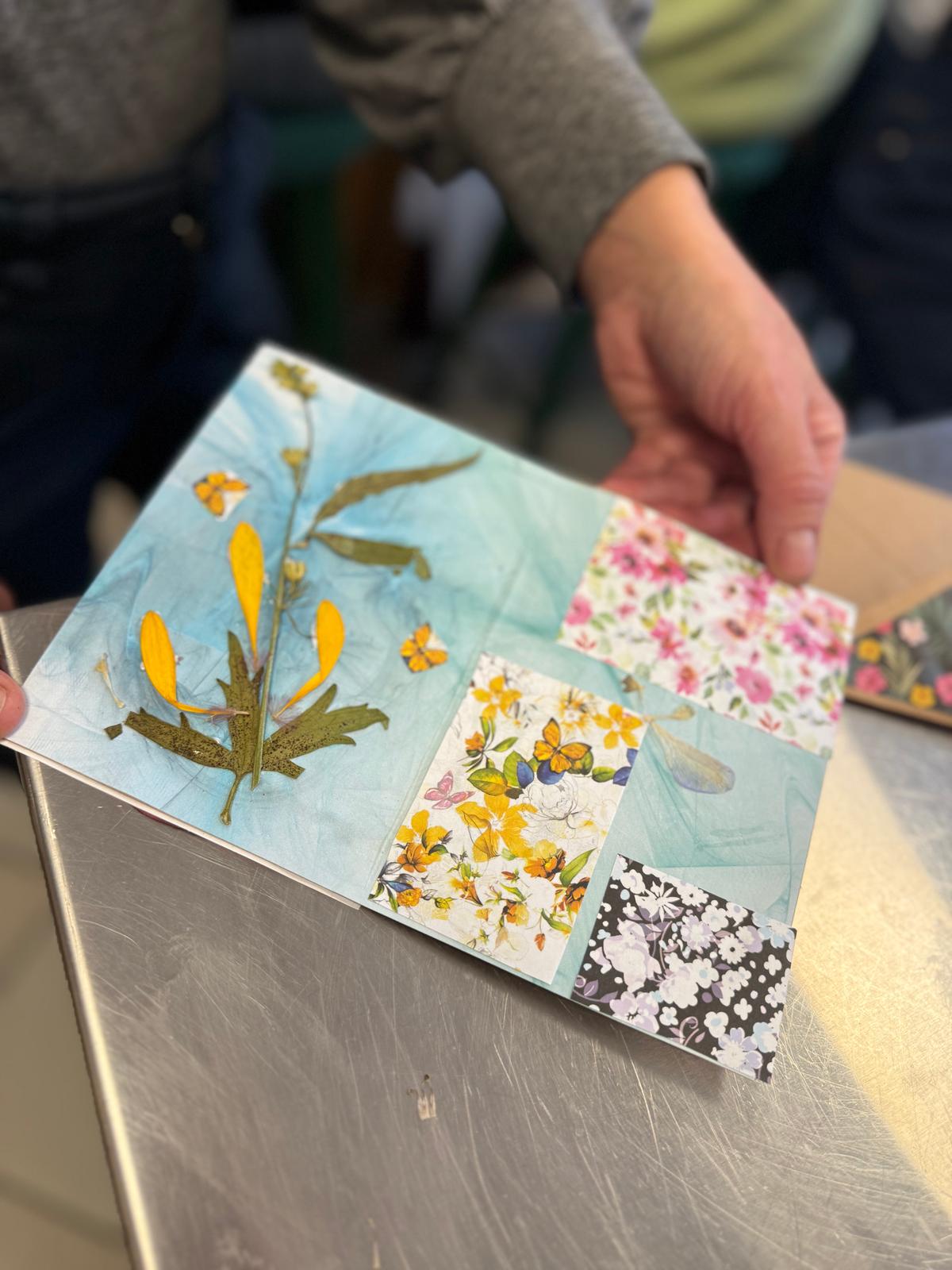 Osoba trzyma rozłożoną kartkę z kwiatowymi wzorami i rysunkami botanicznymi w żółtych i różowych kolorach.