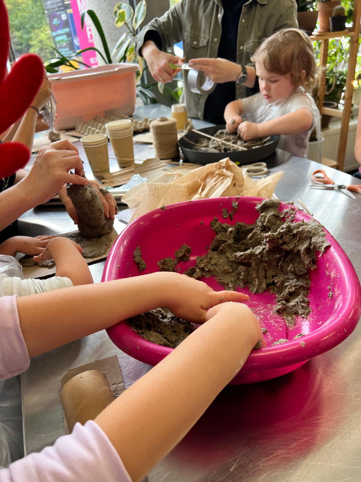 Dzieci bawią się ziemią i glną podczas warsztatu plastycznego w wewnętrznym ogrodzie.