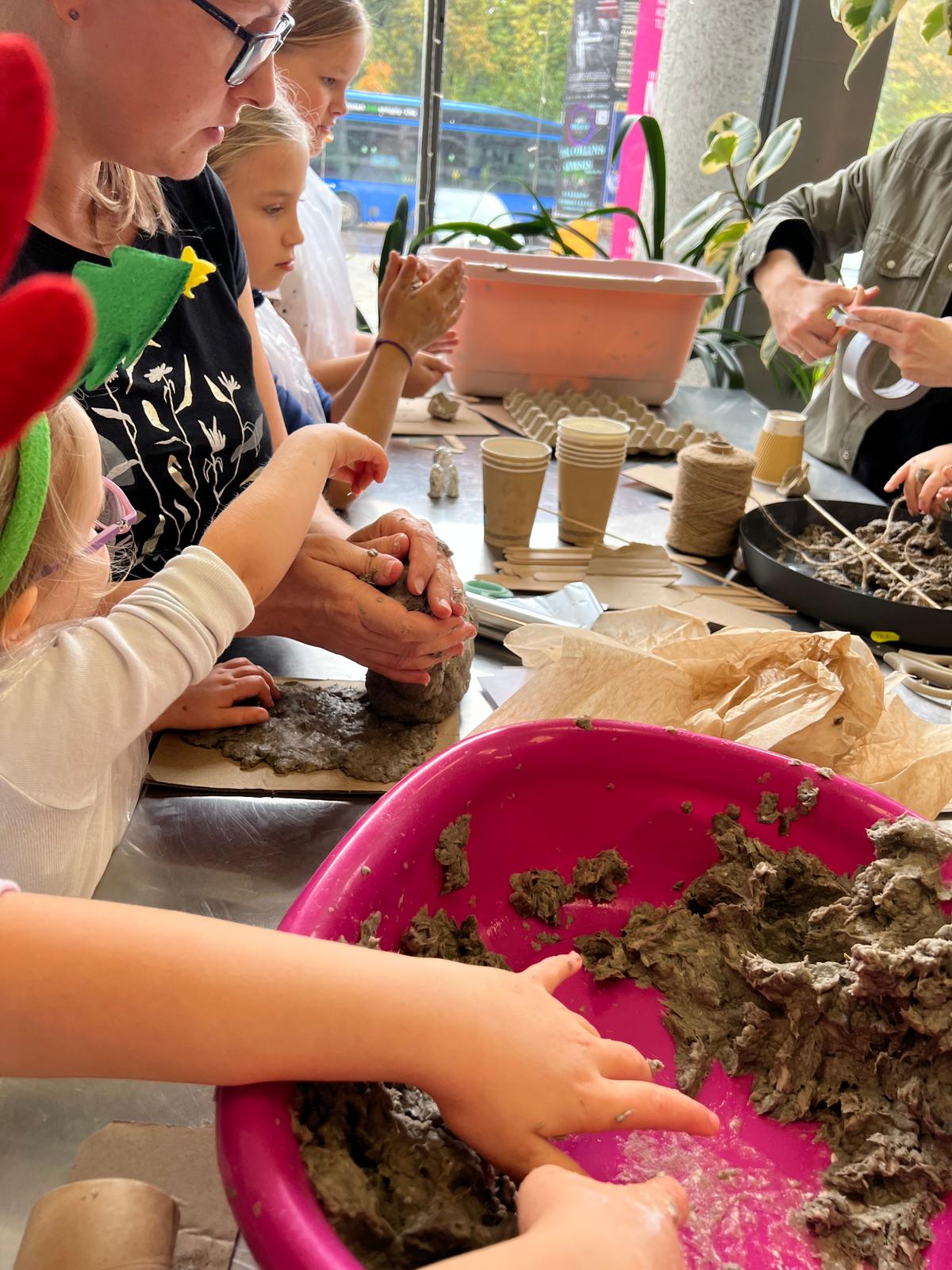 Grupa dzieci bawi się i uczy podczas warsztatu o roślinach, pracując z ziemią i sadzonkami w doniczkach.