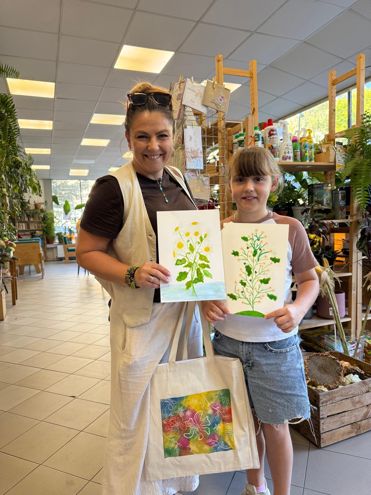 Kobieta i dziewczyna prezentują swoje rysunki roślin w sklepie ogrodniczym, uśmiechając się do aparatu.