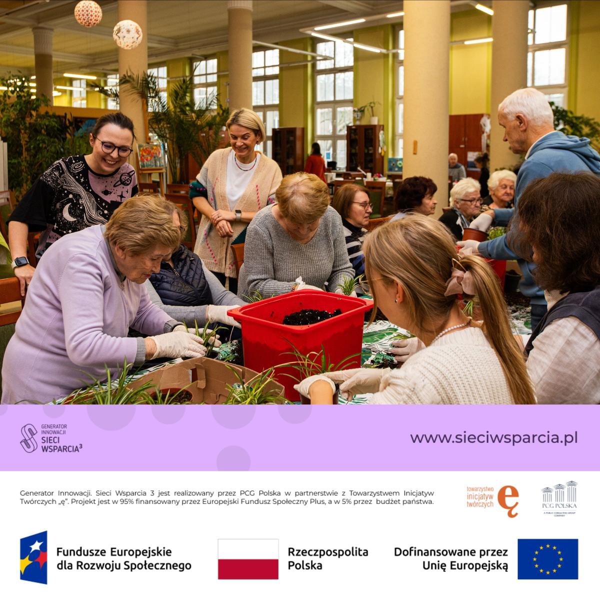 Grupa ludzi różnych pokoleń bierze udział w warsztacie sadzenia roślin w jasnej, nowoczesnej sali.